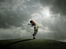 Woman stretching on rock against cloudy sky